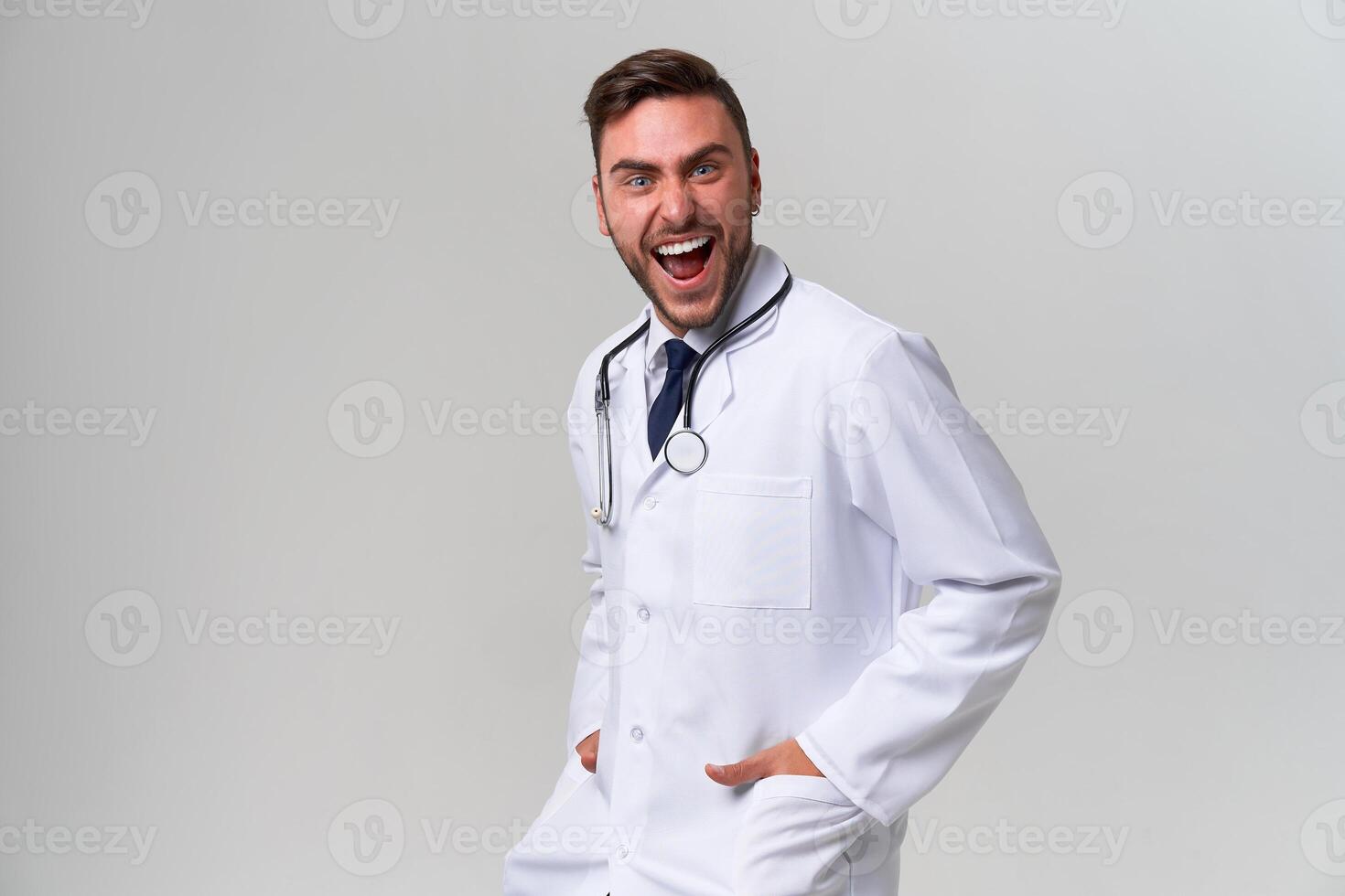 Young handsome modern doctor in a white medical gown stands in the studio on a white background. Student trainee of a medical university. photo