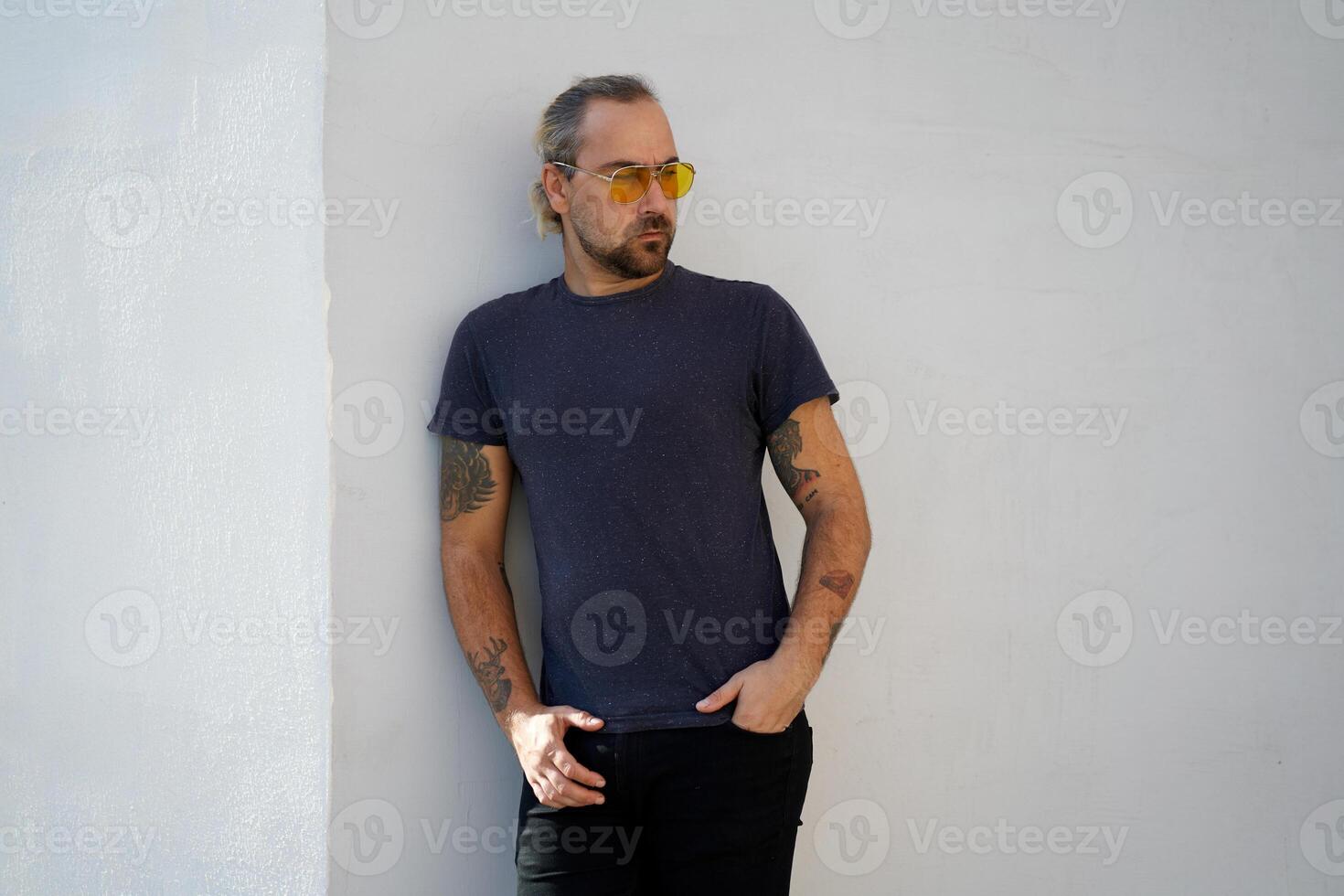 Handsome young unshaven man blue shirt yellow sunglasses stands near white walls summer day. With free copy space for your text photo