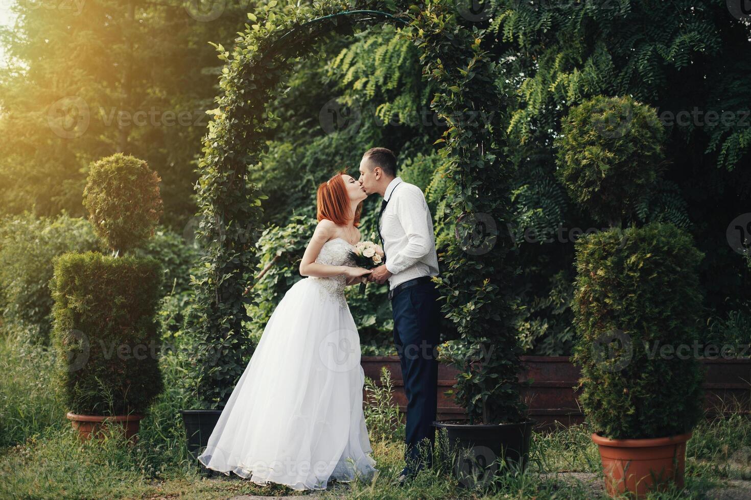 Handsome groom holds the bride's hand near green flower archway photo