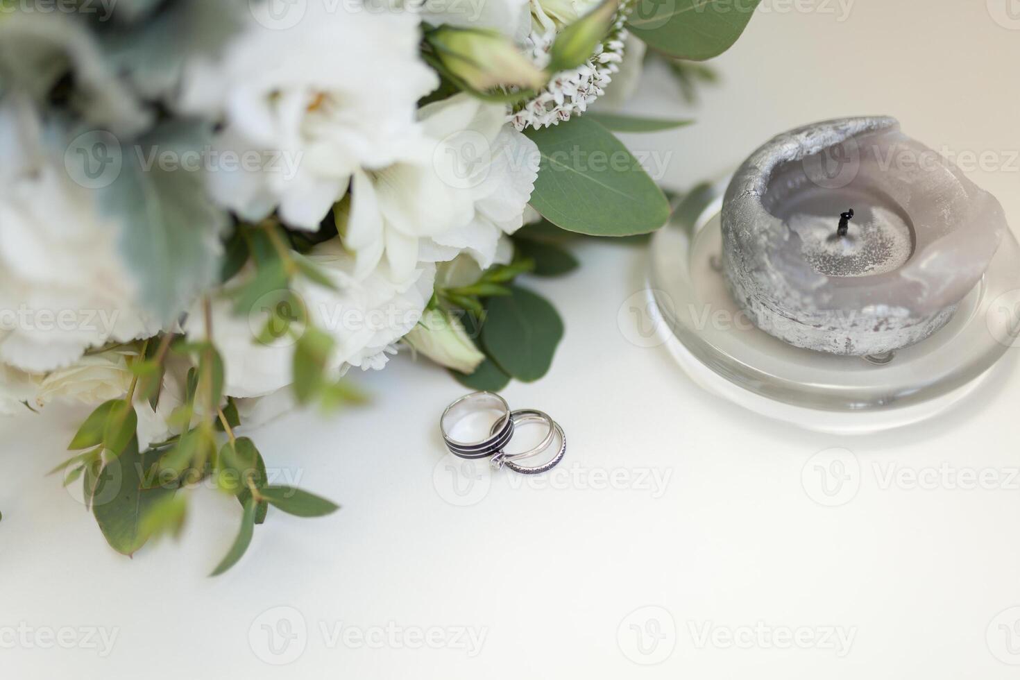 cerca arriba de Boda anillos en antecedentes de blanco flores y vela foto