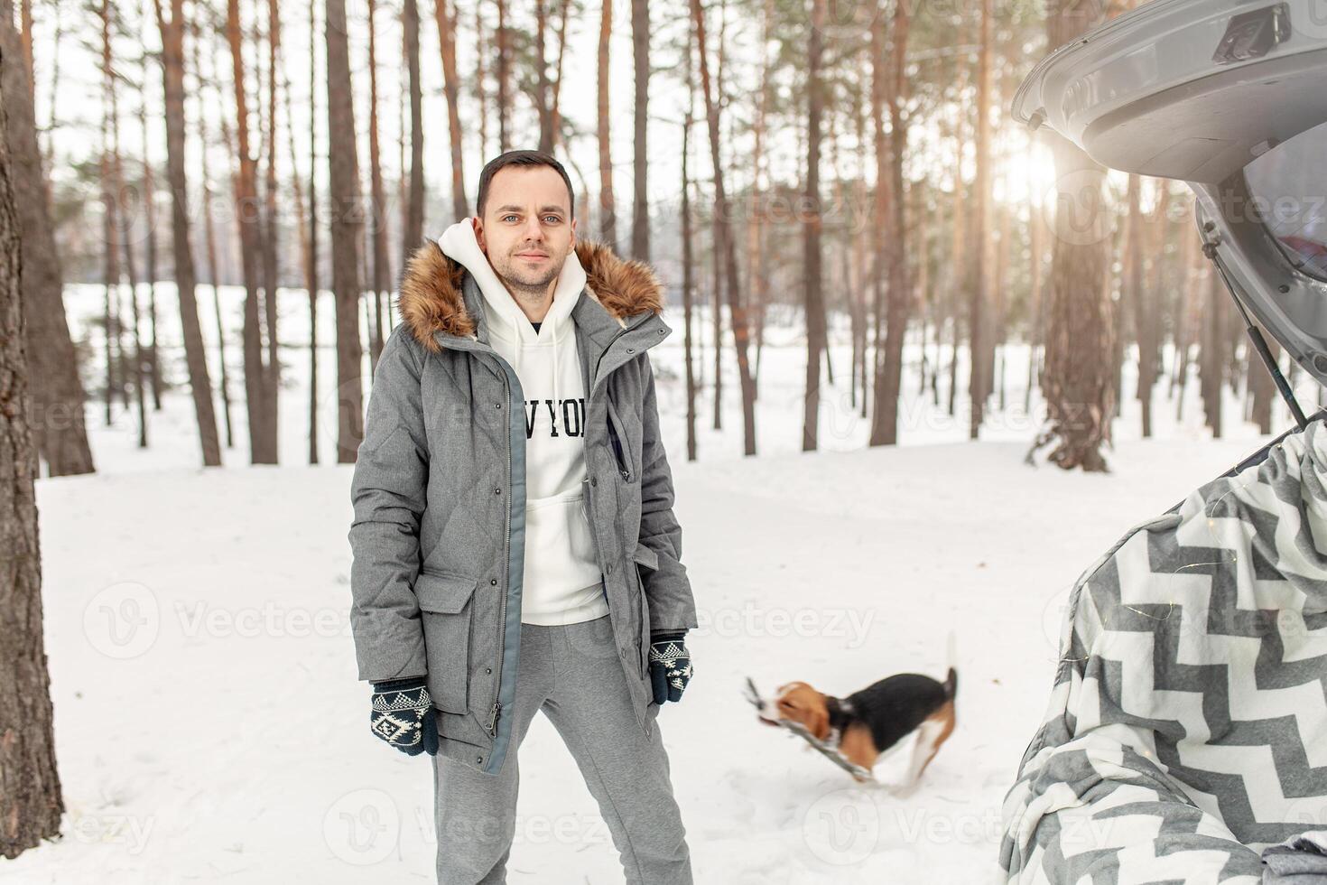 un joven hombre vestido en un gris invierno parque en un Nevado invierno bosque con beagle. concepto acerca de invierno ocio y amor a animales foto