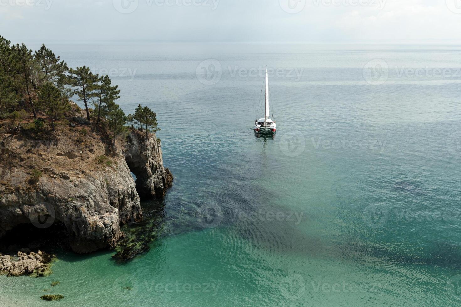 Panoramic view of Pacific Ocean blue transparent water, a white sport modern luxury yacht sail boat floating and a green shore with forest, hills. Holiday by the water and sail race. photo