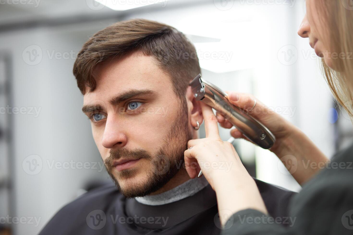 hermoso azul ojos hombre sentado en Barbero tienda. estilista peluquero mujer corte su cabello. hembra Barbero. foto