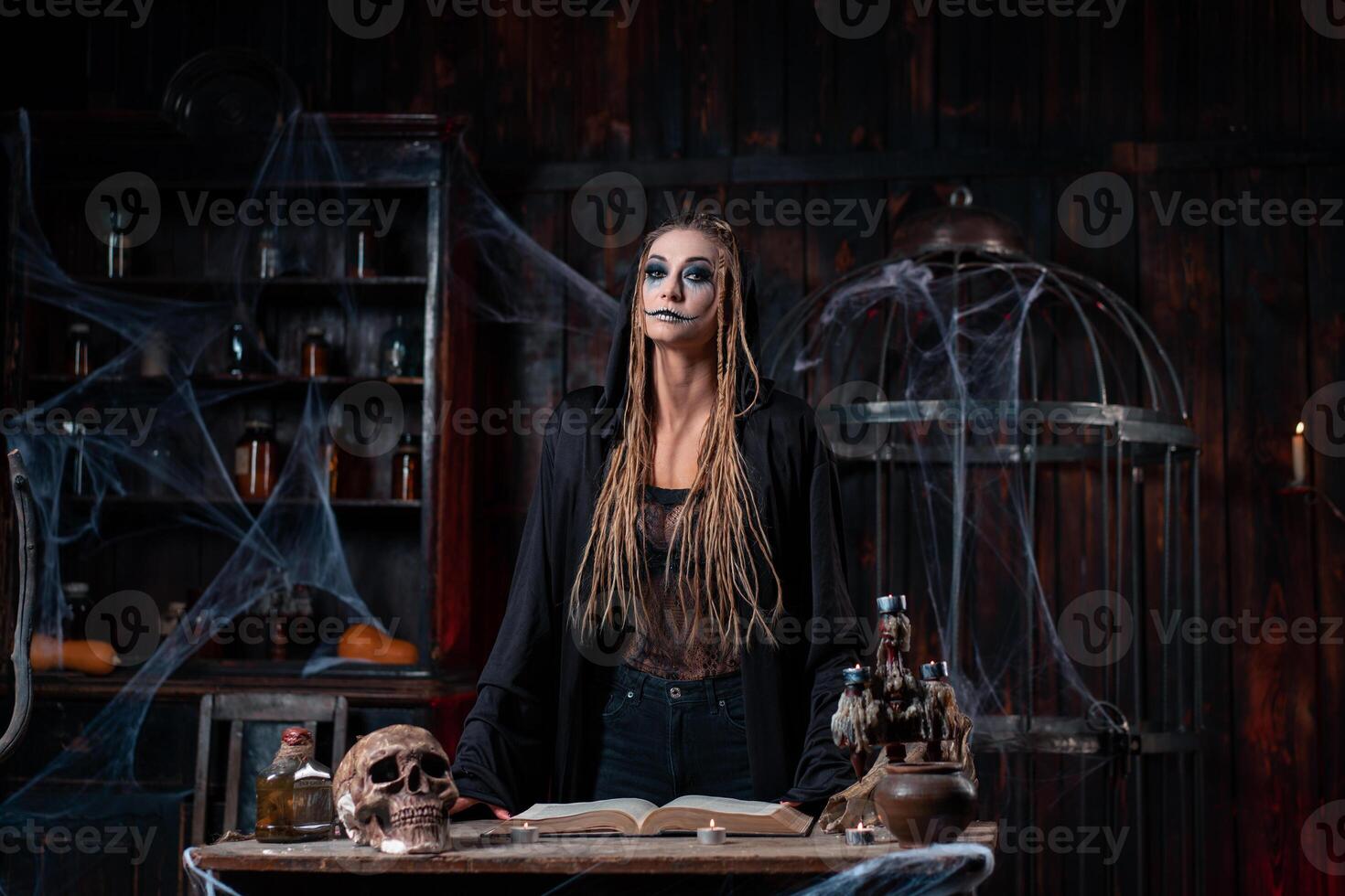 Halloween concept. Witch dressed black hood with dreadlocks standing dark dungeon room use magic book for conjuring magic spell photo