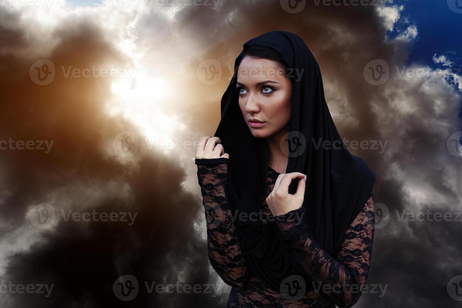 A woman is a prophet sorcerer and a preacher in a black mystical cloak with a hood against a dramatic background... photo