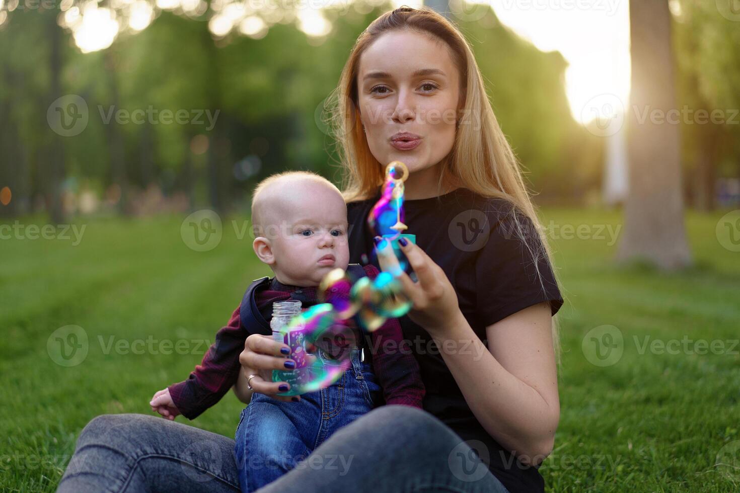 joven caucásico madre infla jabón burbujas con su pequeño hijo en un parque en un soleado verano día. foto