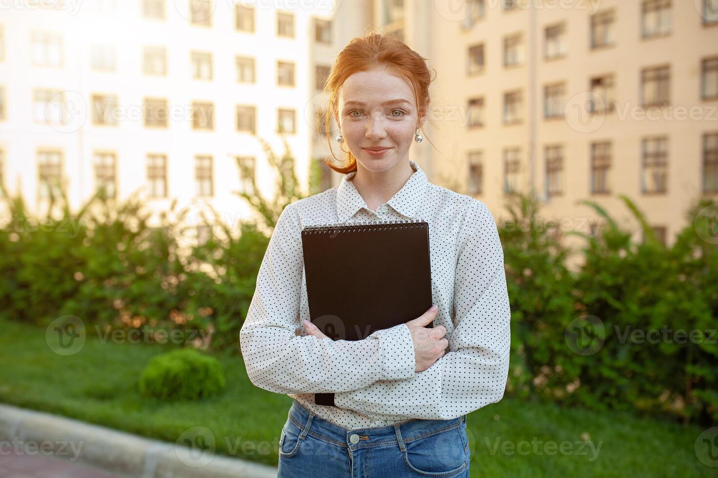 Beautiful red haired girl with freckles hugging notebooks with homework and smiling happy. Back to school concept. Portrait of a student photo