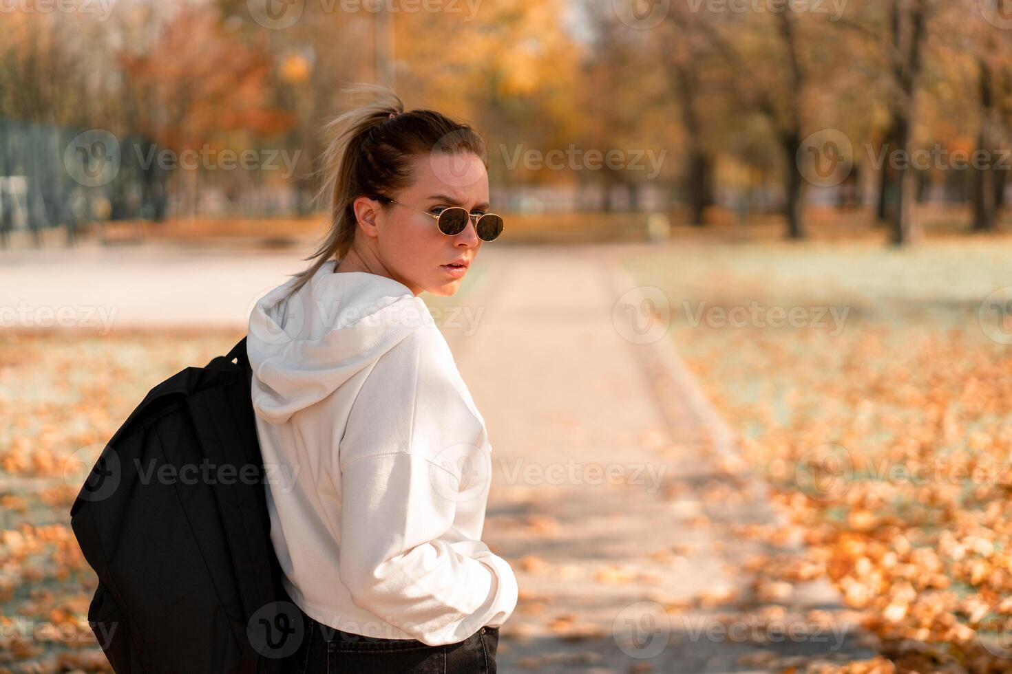 A young beautiful woman with a ponytail and sunglasses, with a backpack on his shoulders in the park. Photo from the back