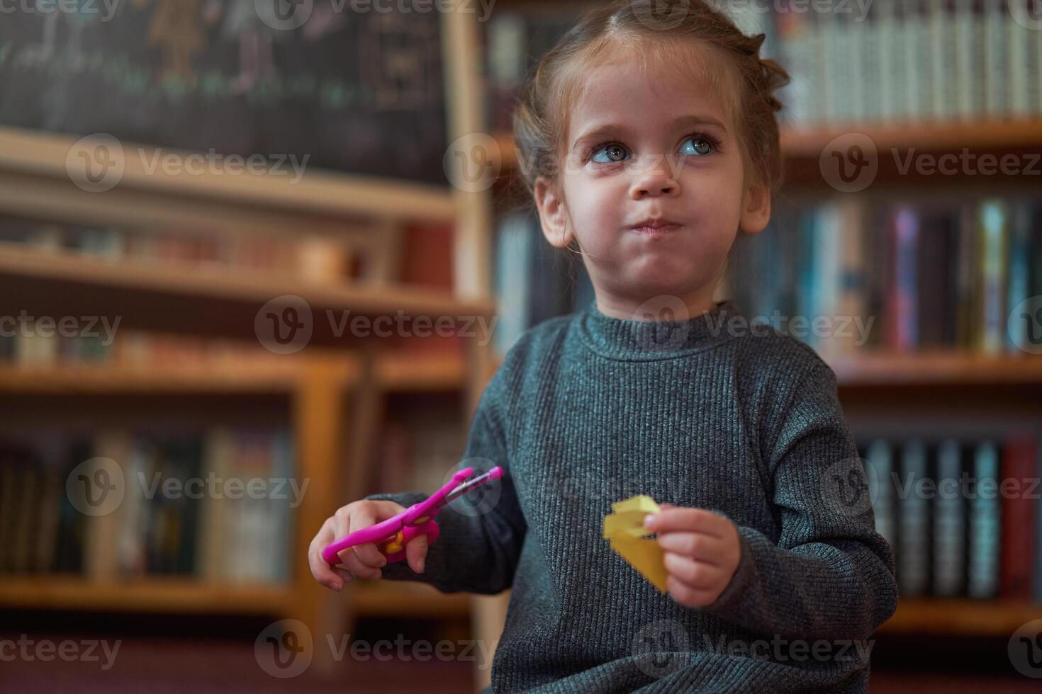 Cute little caucasian girl is playing with scissors and colored paper while sitting on the floor at home. photo