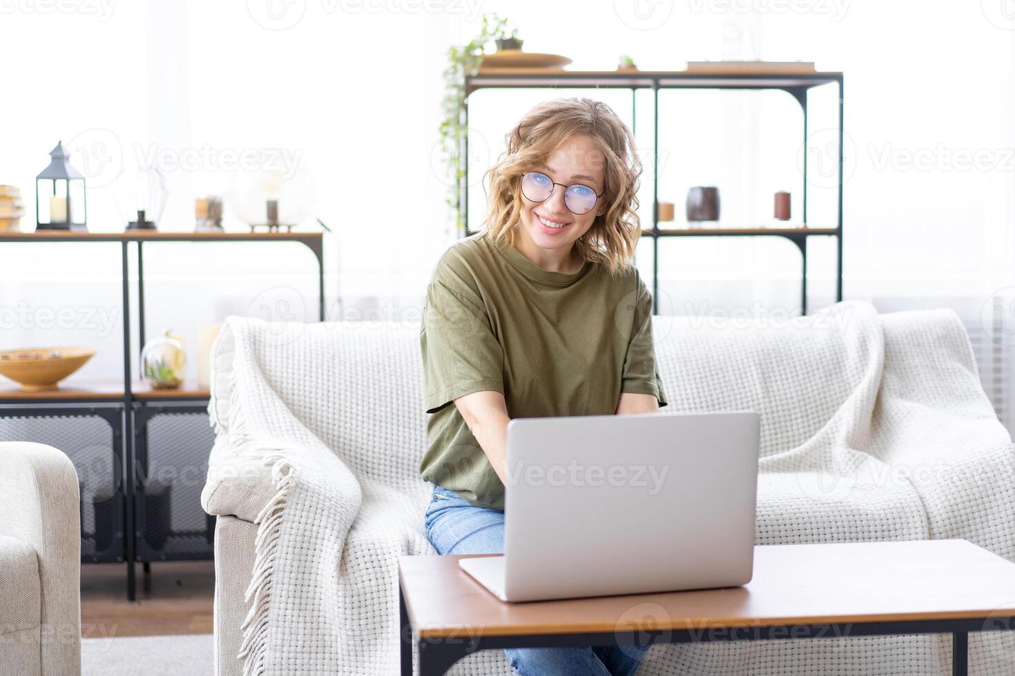 Woman glasses using laptop computer while sitting sofa with big window on background at home interior photo