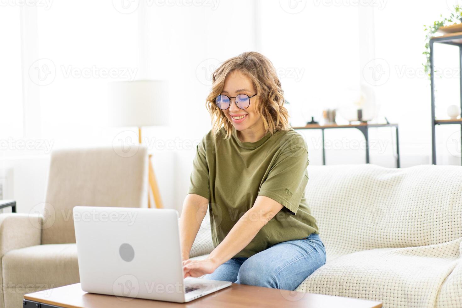 Woman glasses using laptop computer while sitting sofa with big window on background at home interior photo
