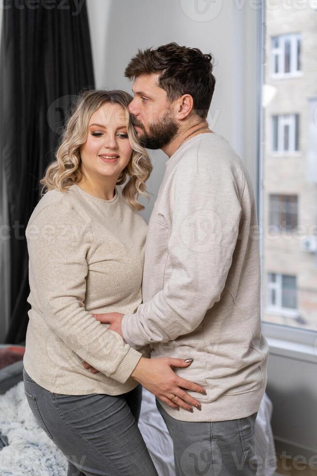 Happy family concept. Husband hug belly pregnant wife standing indoor living room near sofa photo