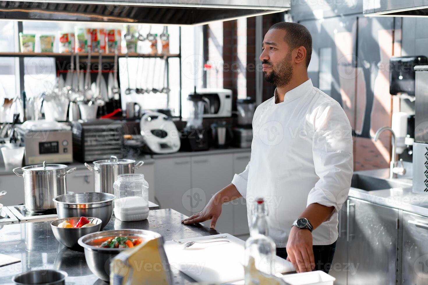 The chef conducts a master class in cooking. On the background is kitchen utensils, on the table in front of him vegetables in bowls photo