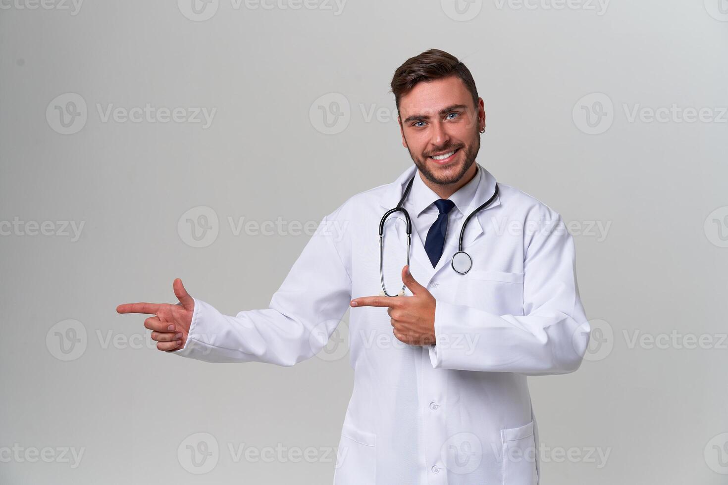 Young handsome modern doctor in a white medical gown stands in the studio on a white background. Student trainee of a medical university. photo