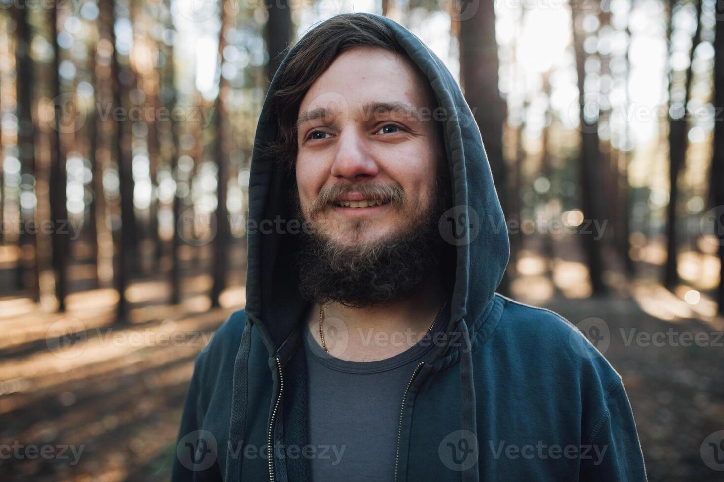 cerca arriba retrato de un barbado hipster turista en gris capucha hombre en el luz de sol bosque bosque foto