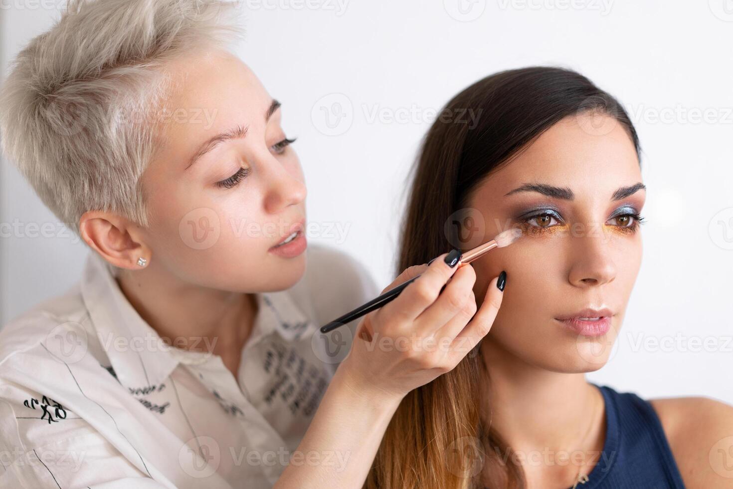 Make-up artist applying bright base color eyeshadow on model's eye and holding a shell with eyeshadow on background photo