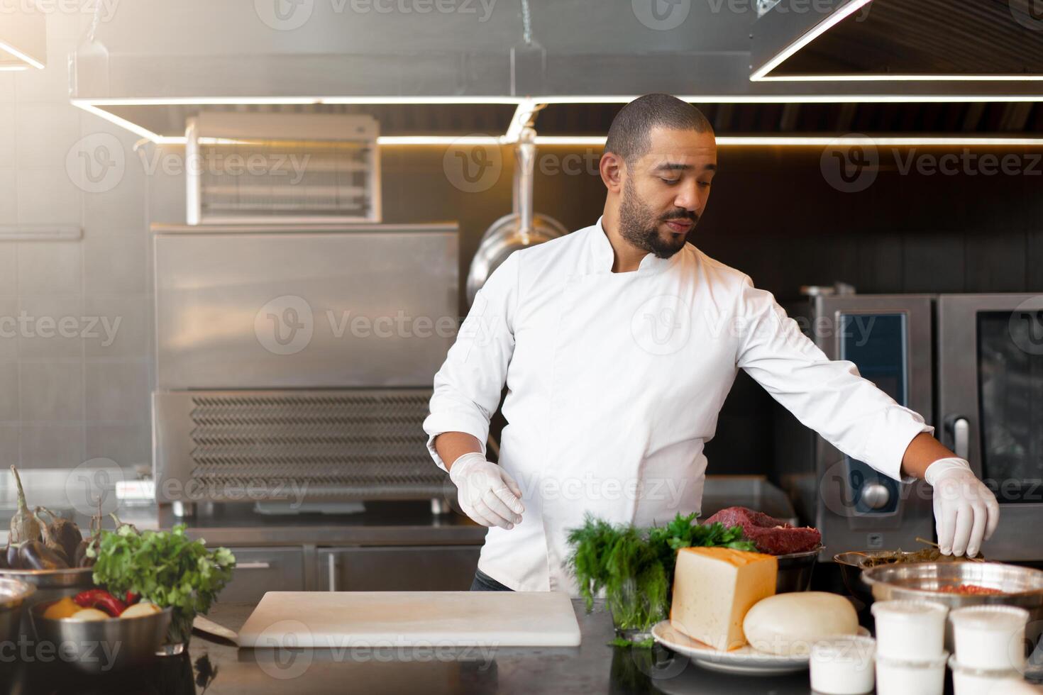 hermoso joven africano cocinero en pie en profesional cocina en restaurante preparando un comida de carne y queso vegetales. foto