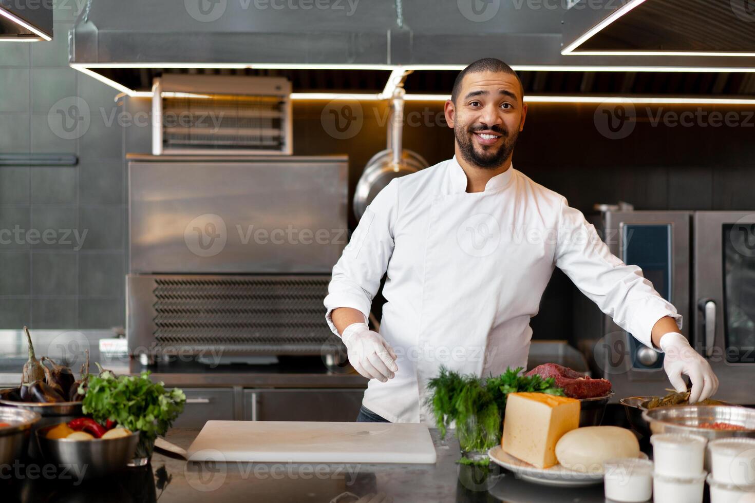 hermoso joven africano cocinero en pie en profesional cocina en restaurante preparando un comida de carne y queso vegetales. foto