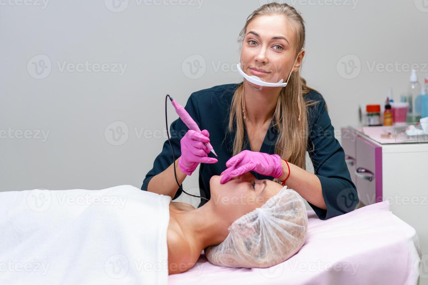 Cosmetology cabinet client lies on couch. Beautician applies marking on eyebrows. photo