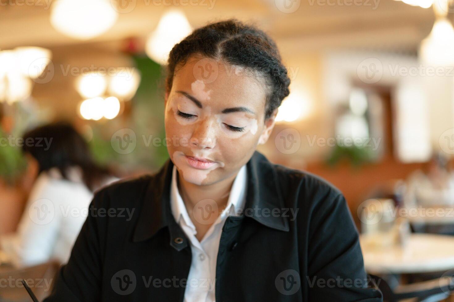 un hermosa joven niña de africano etnia con vitiligo sentado en un restaurante foto