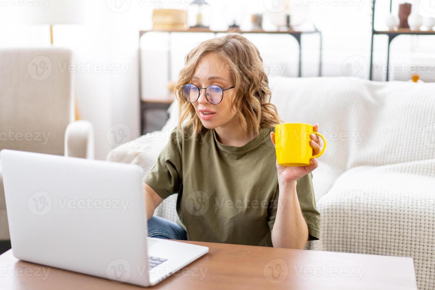 Woman glasses using laptop computer while sitting near sofa with big window on background at home interior photo