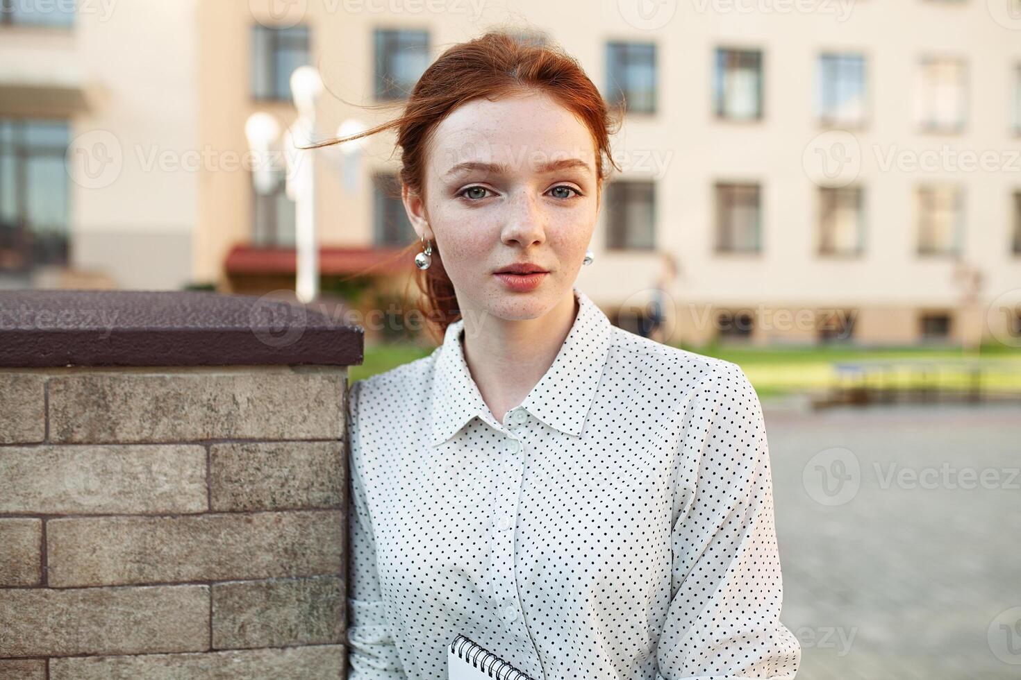 Beautiful red haired girl with freckles hugging notebooks with homework and smiling happy. Back to school concept. Portrait of a student photo