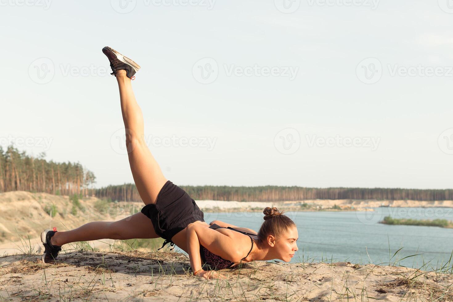 An attractive young woman doing a yoga pose for balance and stretching near the lake high in the mountains photo
