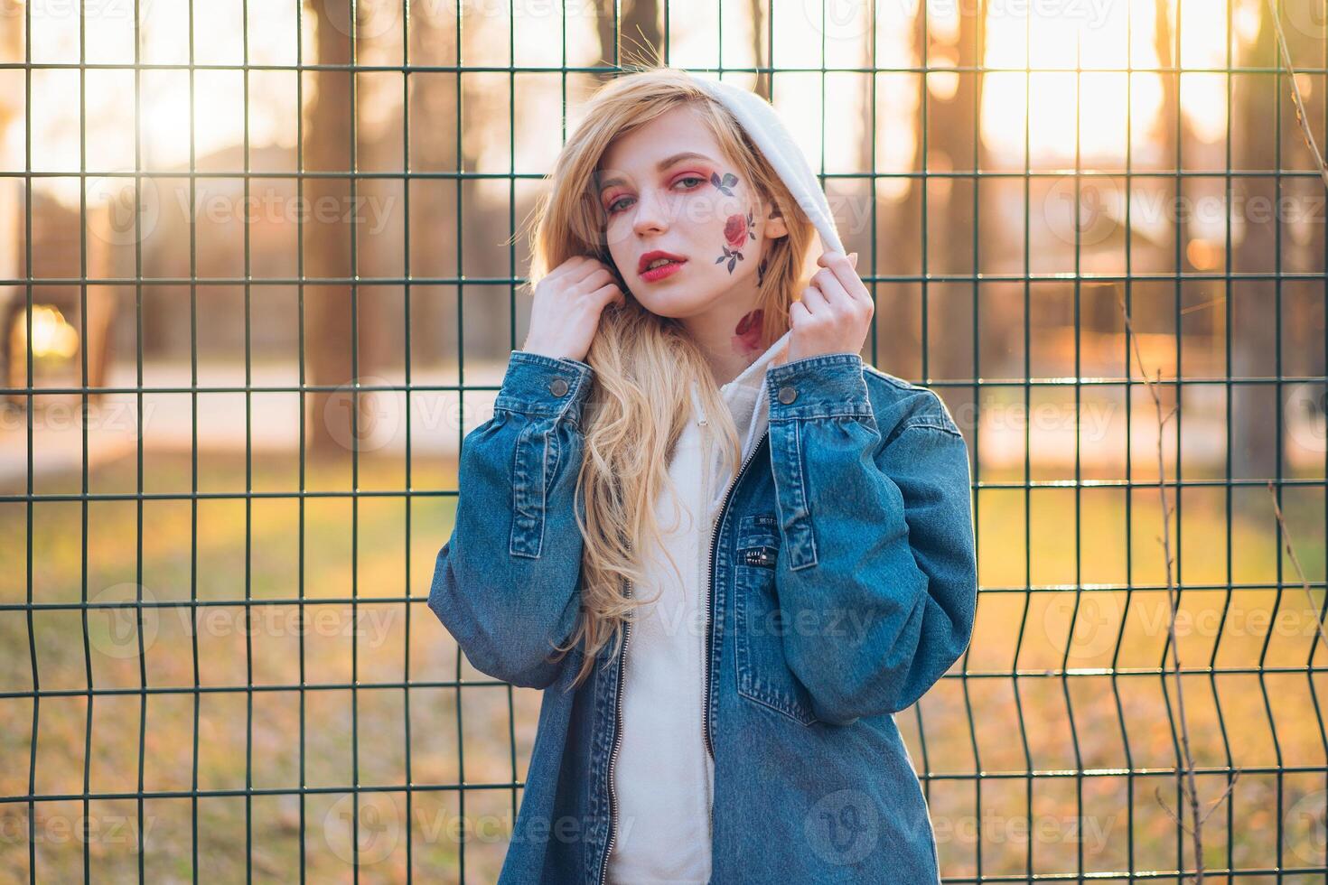 Young Woman with temporary painted flowers on the face. teenage girl with long blond hair wear jeans jacket and hoody photo