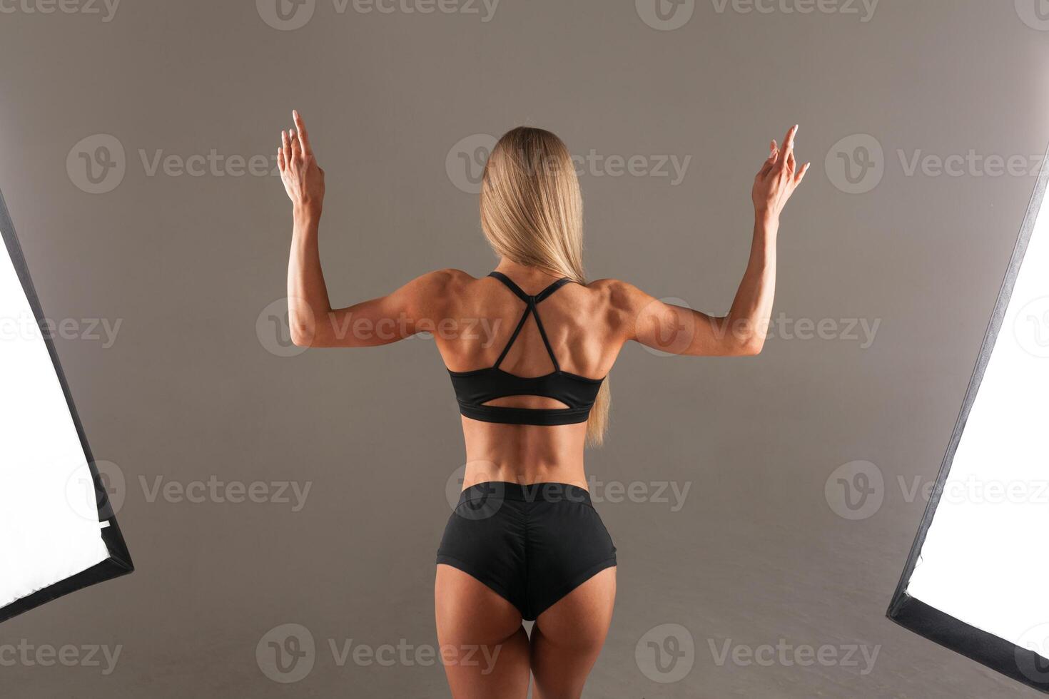 Strong Athletic woman Fitness Model posing back muscles, triceps, latissimus over black background in the studio. Athletic young woman showing muscles of the back and hands. photo