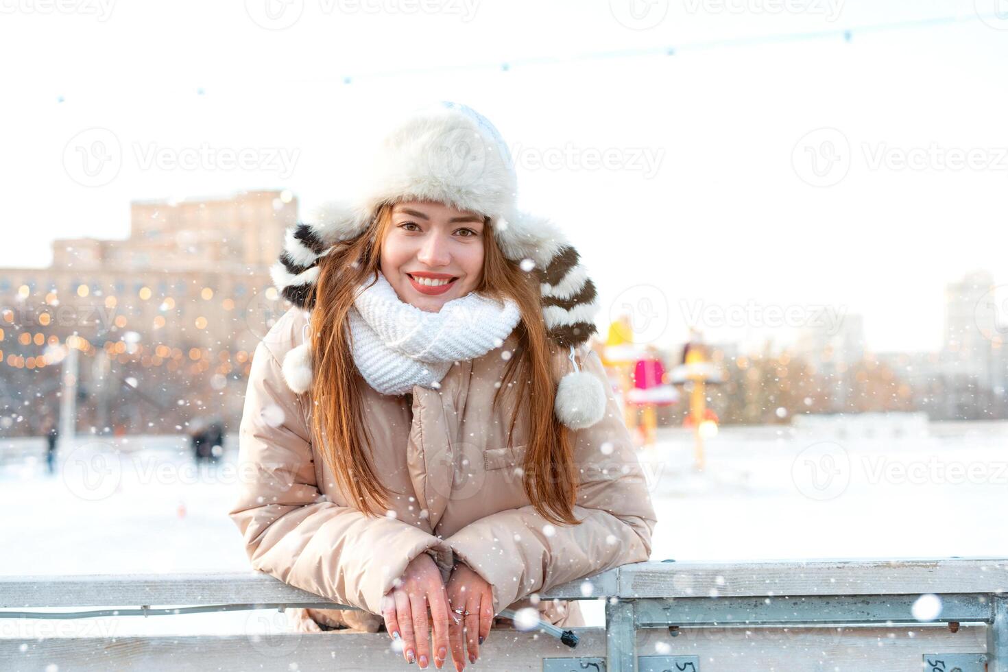 Medium shoot portrait of romantic European lady wears long stylish winter jacket and funny fluffy hat in snowy day. Outdoor photo of inspired blonde woman enjoying winter city.