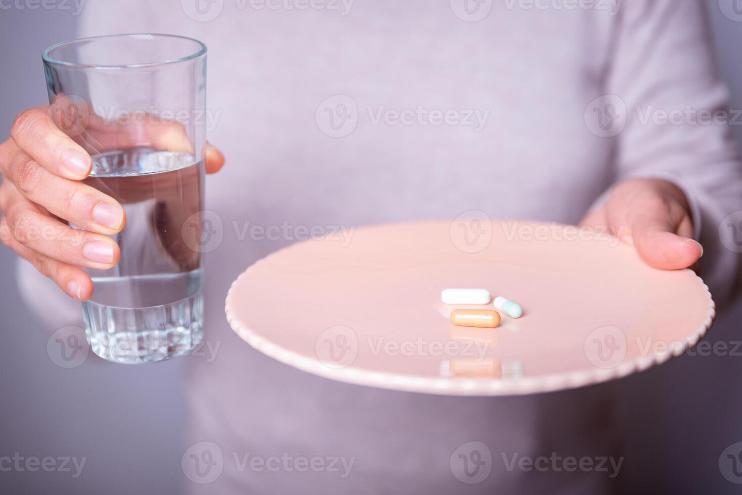 Unrecognizable person with a plate of pills and a glass of water. photo