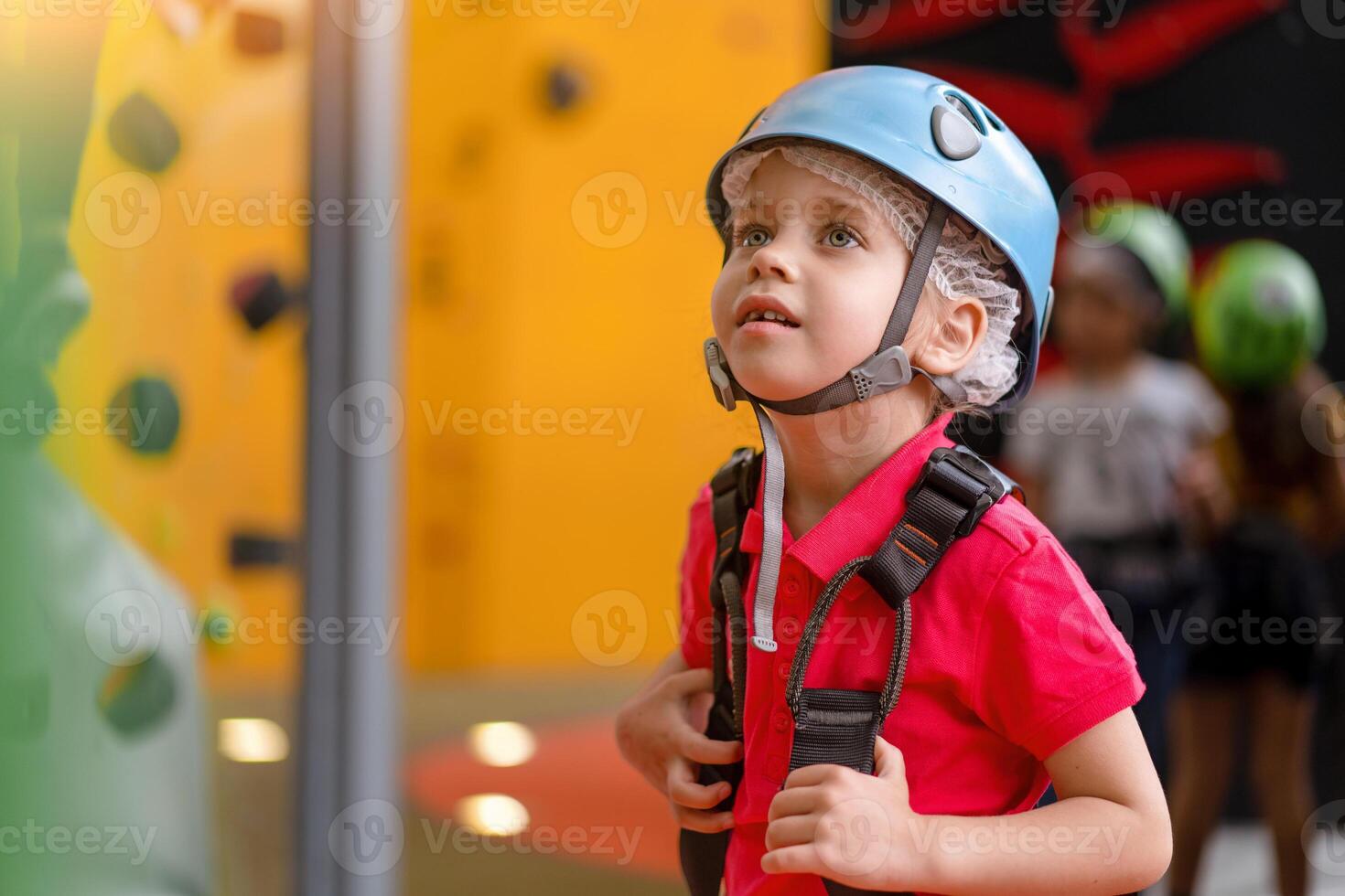Cute little girl climber in blue protective helmet and gear for climbing standing in climber centre amusement park for children photo