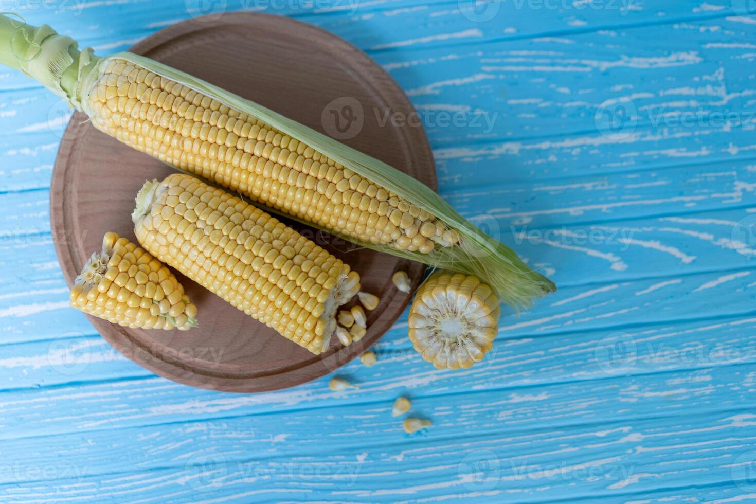 Corn cob with green leaves lies on Round cutting board. blue color background. photo