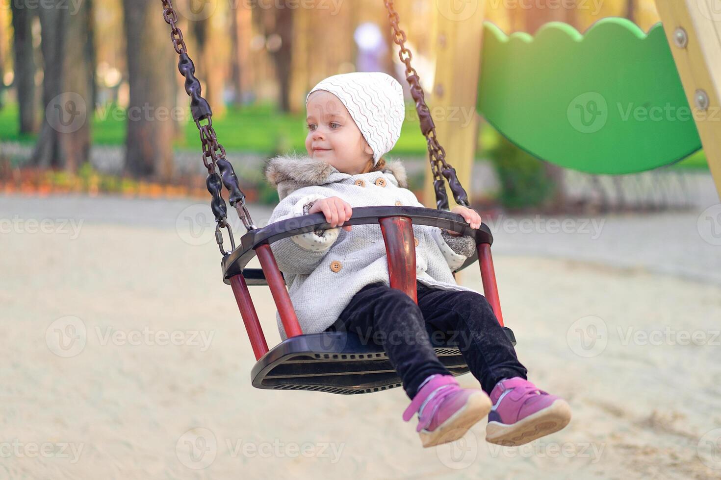 Happy child girl on swing in sunset fall. Little kid playing in the autumn on the nature park photo