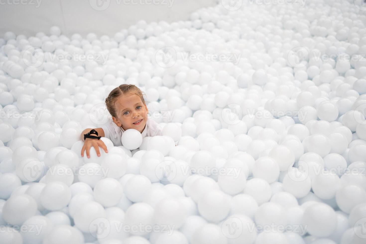Happy little girl playing white plastic balls pool in amusement park. playground for kids. photo