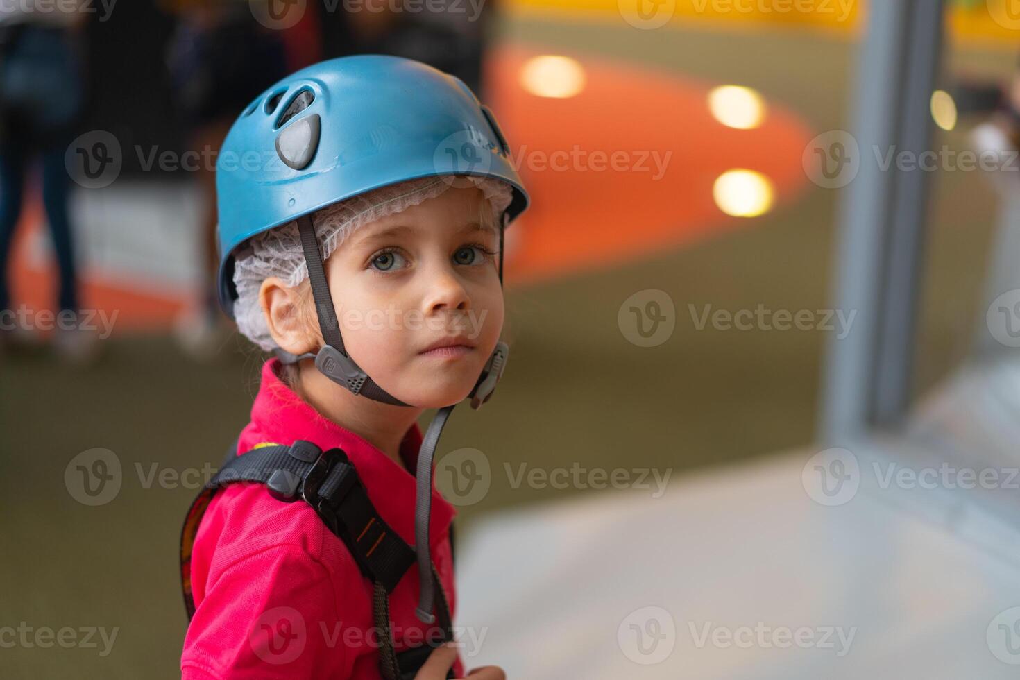 Cute little girl climber in blue protective helmet and gear for climbing standing in climber centre amusement park for children photo