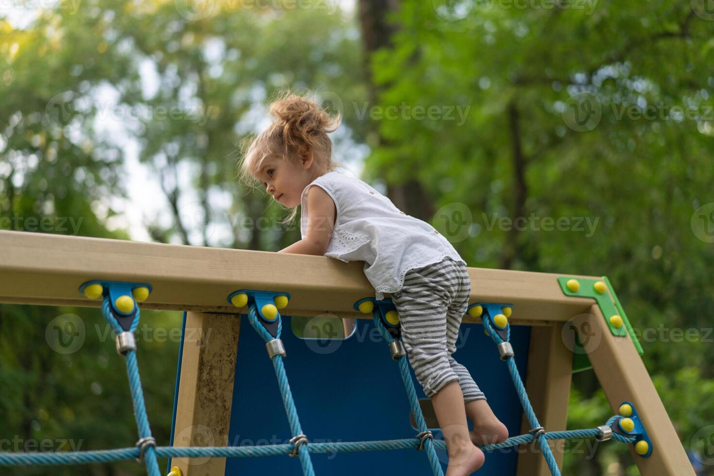 Little Caucasian girl plays on playground climbs stairs upstairs. photo