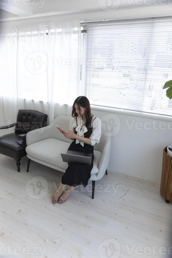 un japonés mujer comprobación teléfono inteligente por remoto trabajo en el pequeño oficina foto