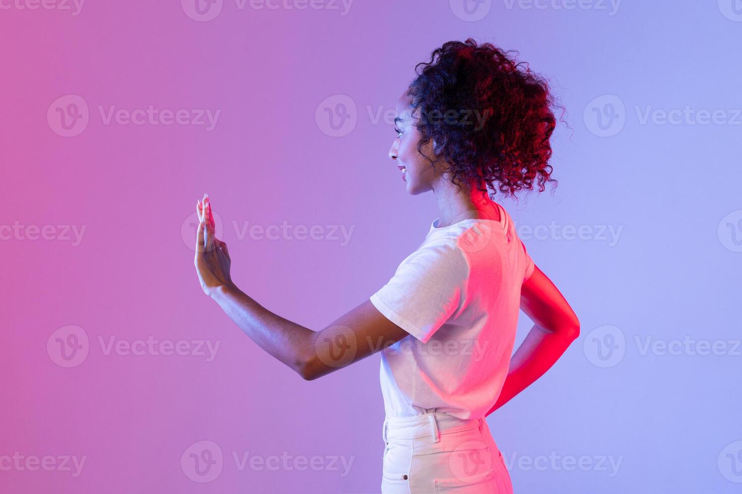 Curly-haired woman gestures at unseen interface, colorful backdrop photo
