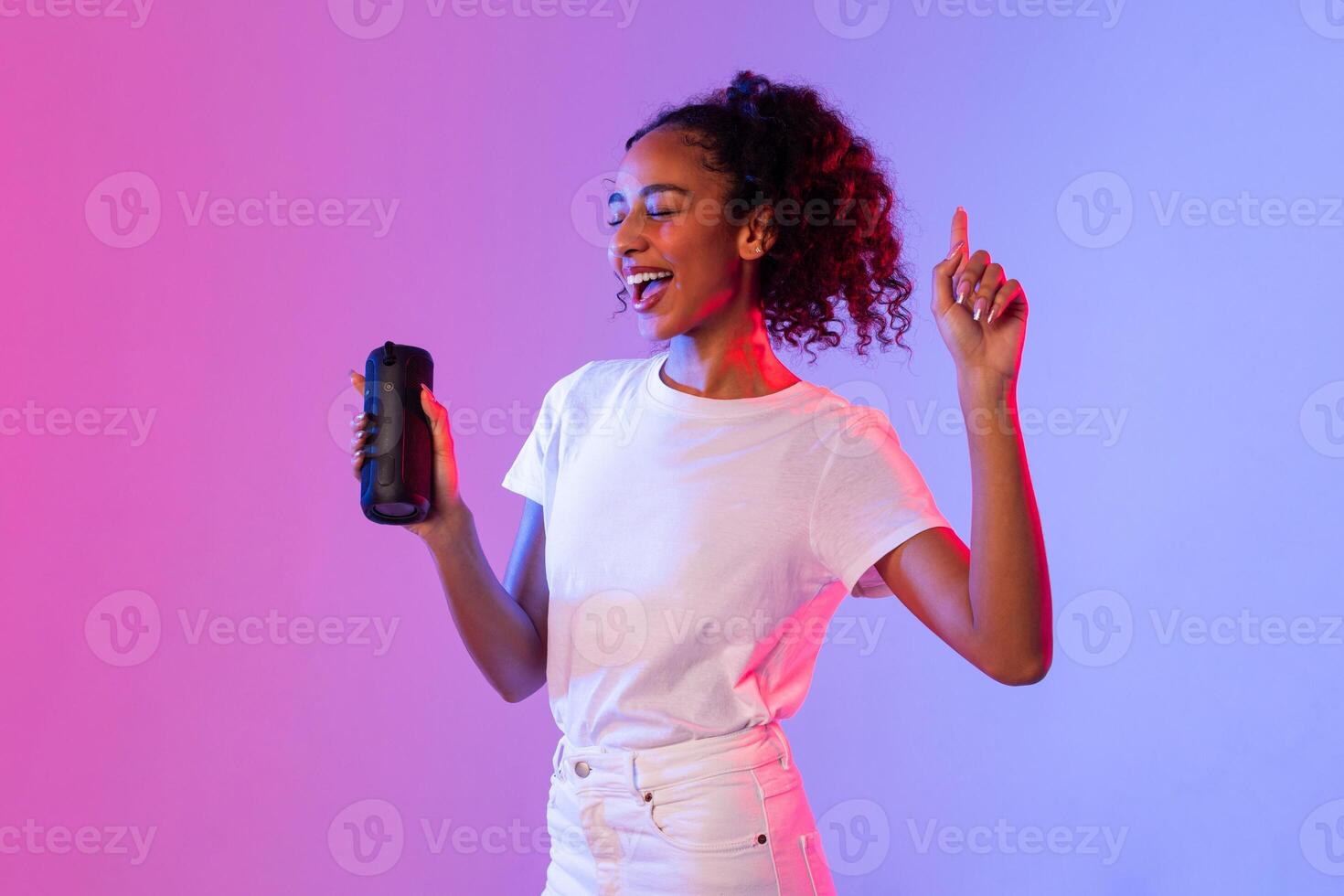 alegre negro dama bailando con portátil altavoz en degradado antecedentes foto