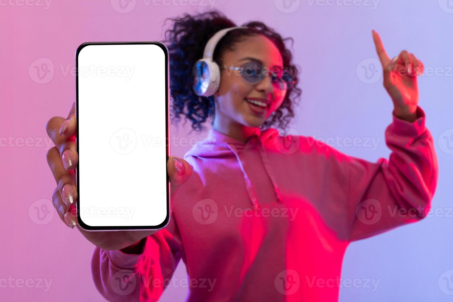 Happy woman with headphones, showcasing smartphone and dancing, colorful background photo