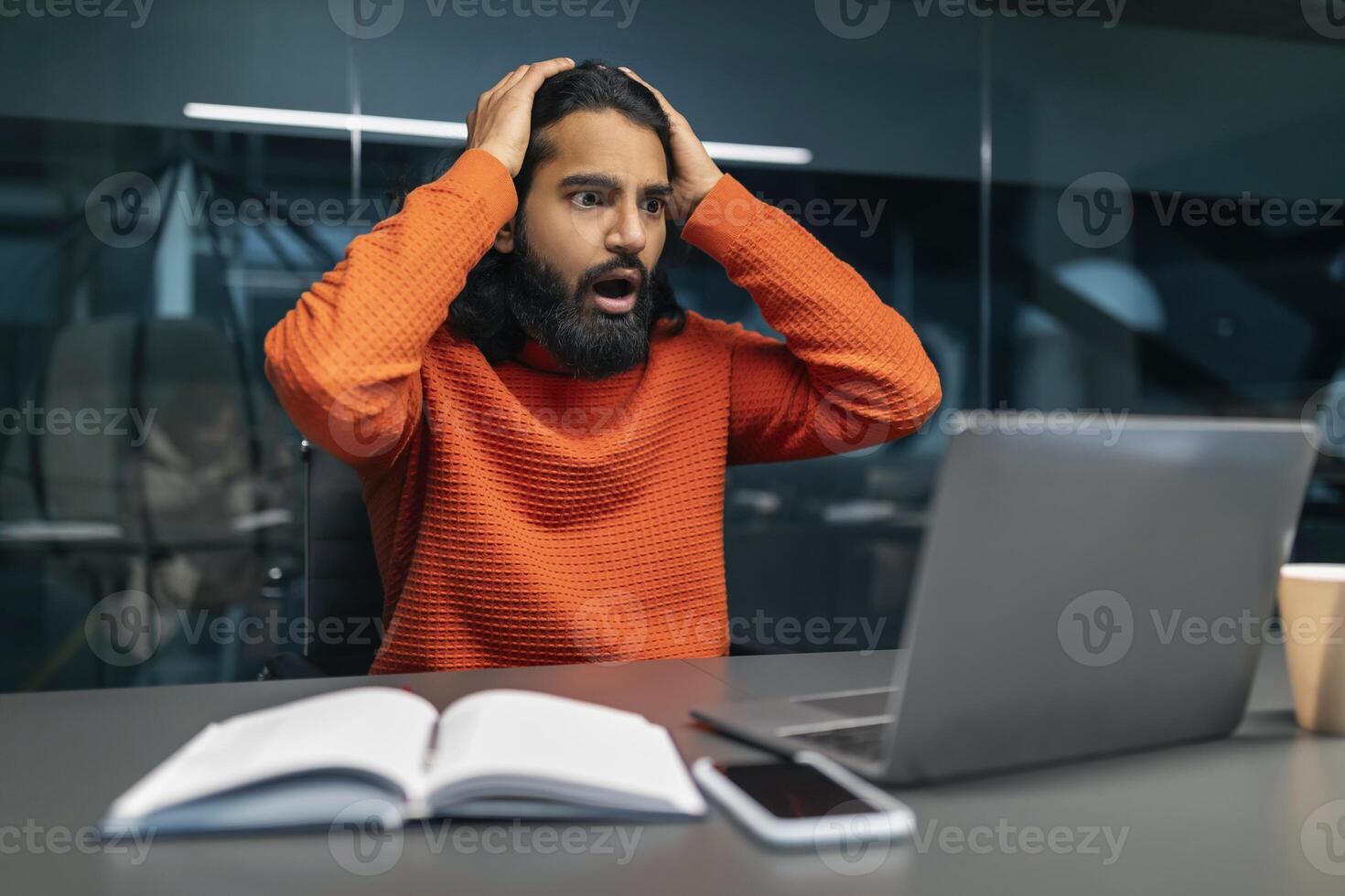 Shocked millennial eastern businessman in dark office photo