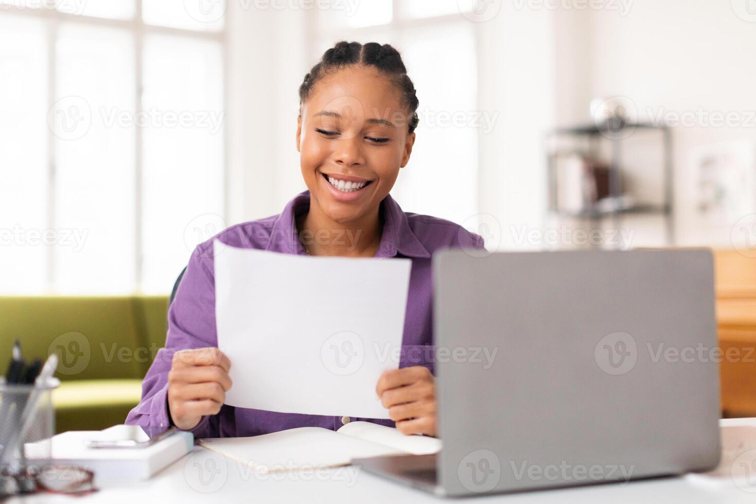 Happy lady student reading paper in front of her laptop photo