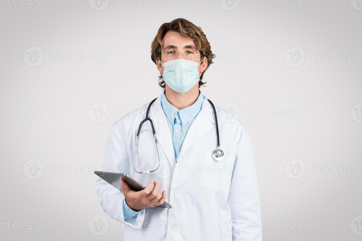 Serious male doctor with mask holding digital tablet photo