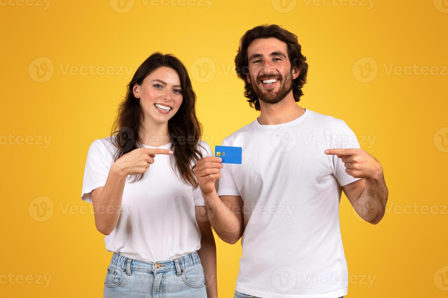 Smiling young couple in casual white t-shirts, the woman pointing at a blue credit card photo