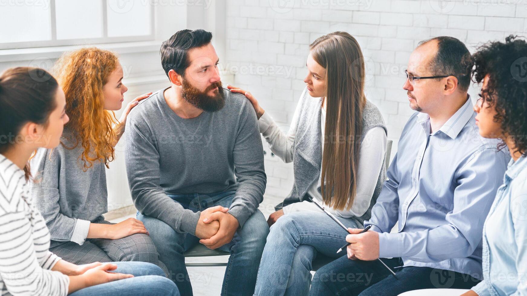 Therapy Group Members Comforting Upset Man On Community Meeting In Rehab photo