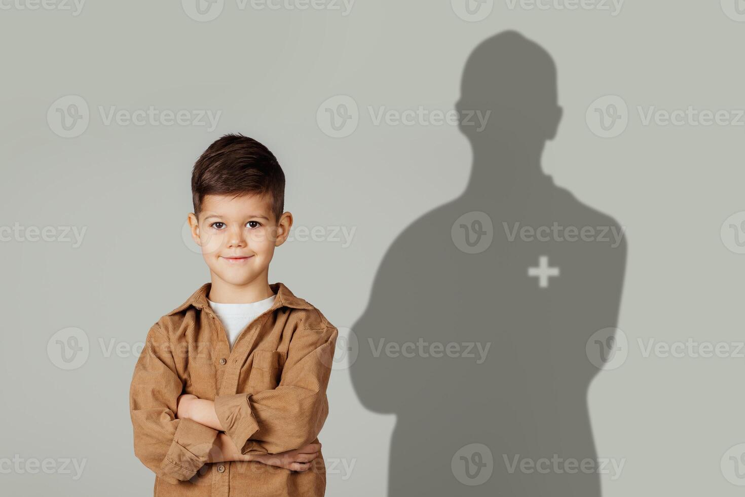 A confident little boy with arms crossed smiles in front of a grey backdrop photo