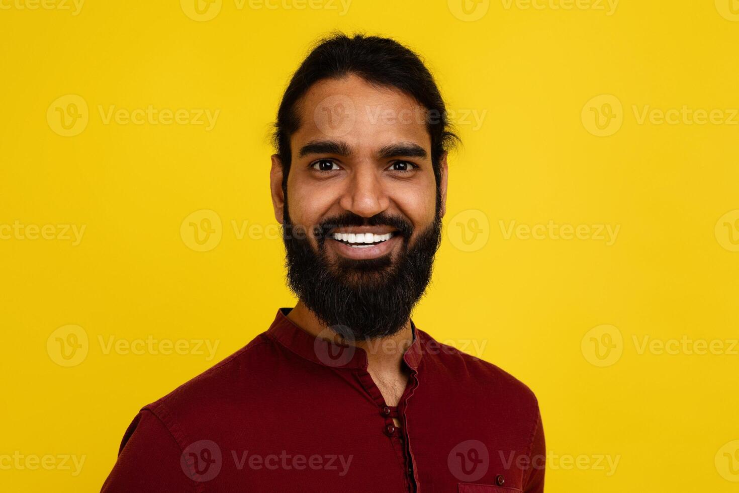 Portrait of millennial bearded indian man posing on yellow photo