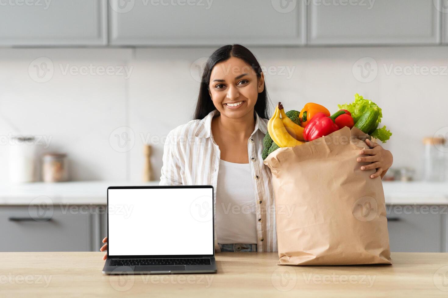 Happy young indian woman order grocery online, showing laptop photo