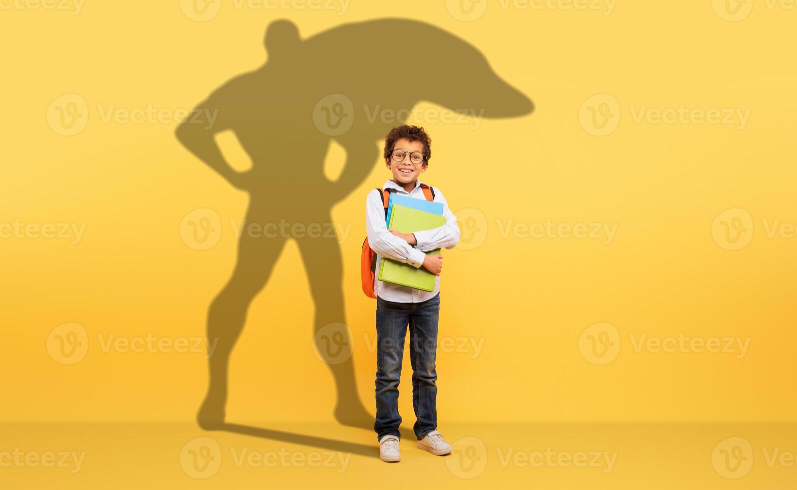 A studious young boy with curly hair and glasses holds his school books tightly photo